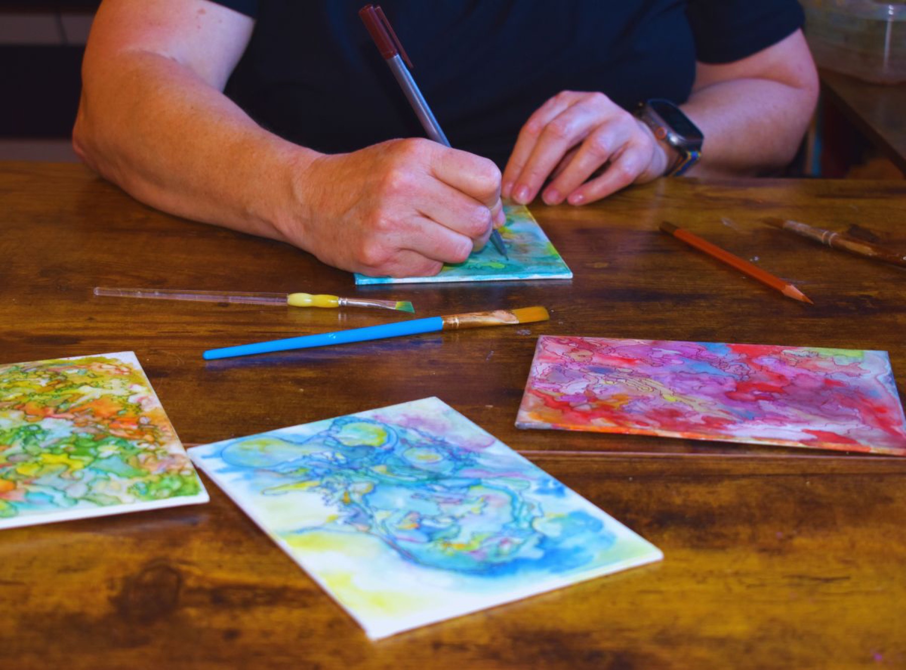 A child's hands mixing watercolor paint at a table during a Creative Sage class